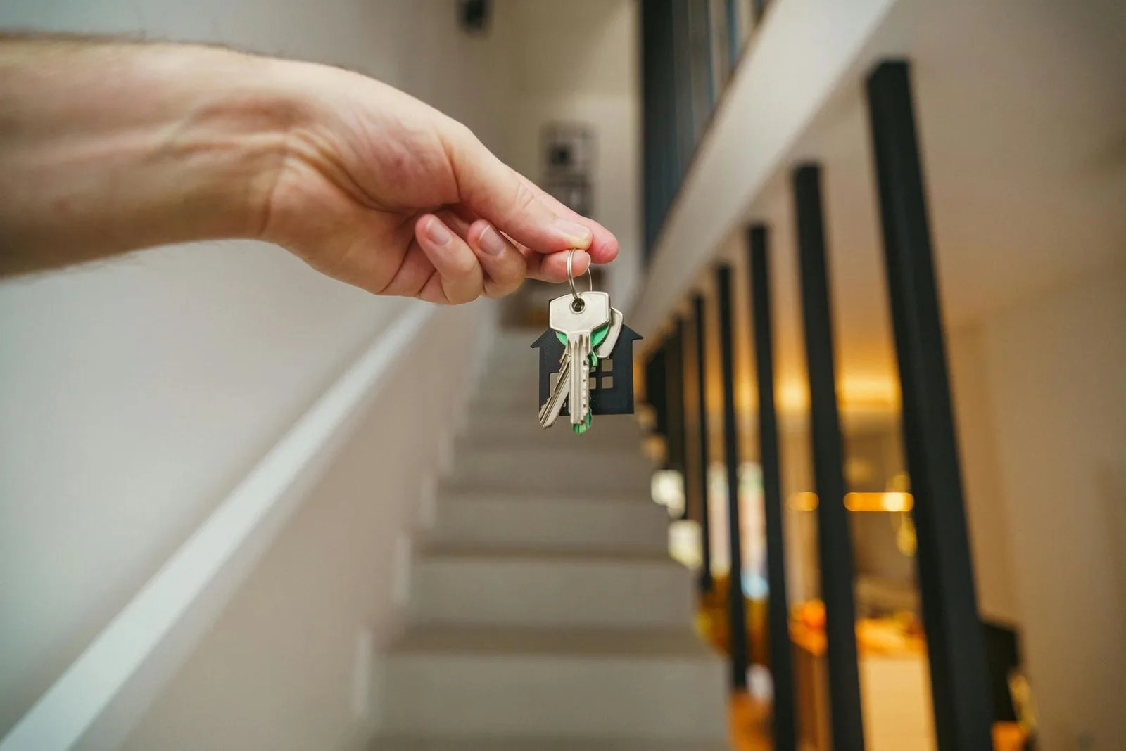Homeowners Insurance Hand holding house keys in front of a staircase, symbolizing homeownership.