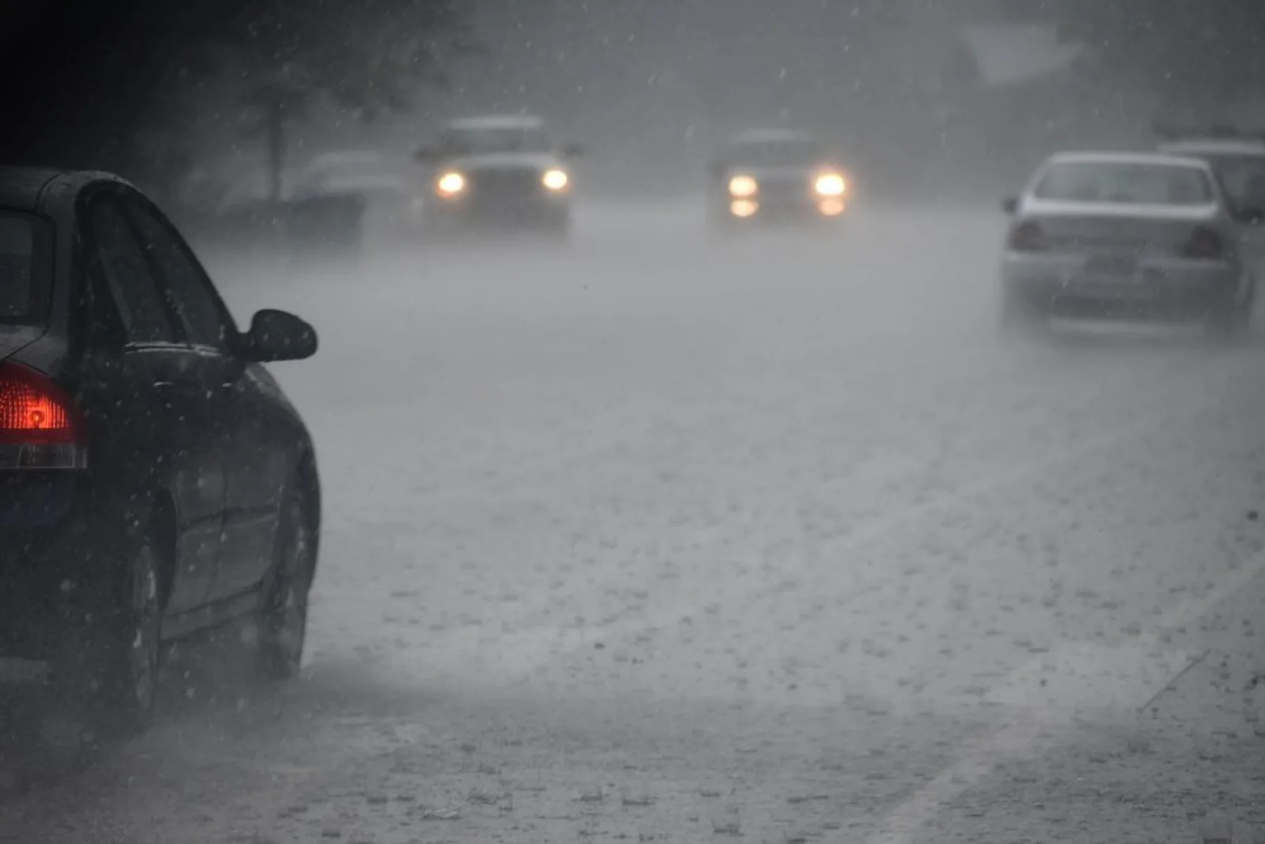 Cars driving on a rain-soaked road with headlights on.